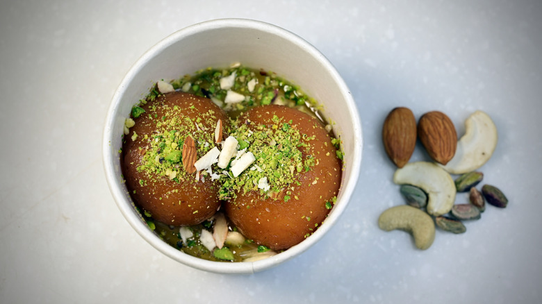 gulab jamun in a white bowl topped with chopped nuts, along with whole nuts on the side