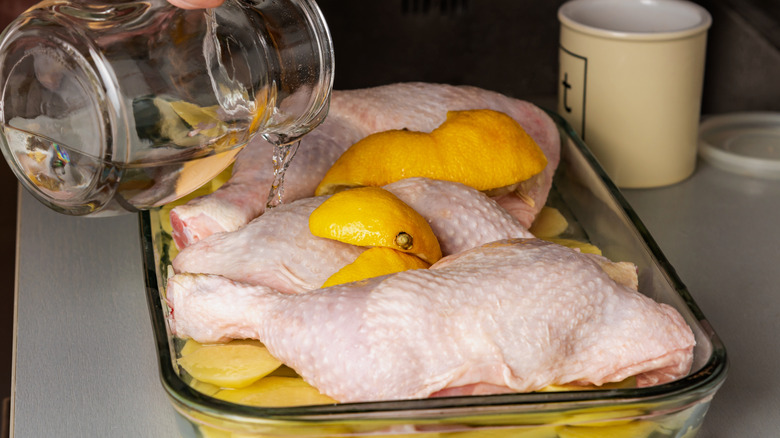 Person adding liquid to glass baking dish with chicken