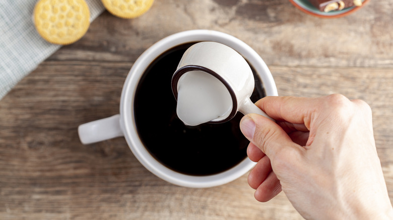 Person pouring cream into coffee