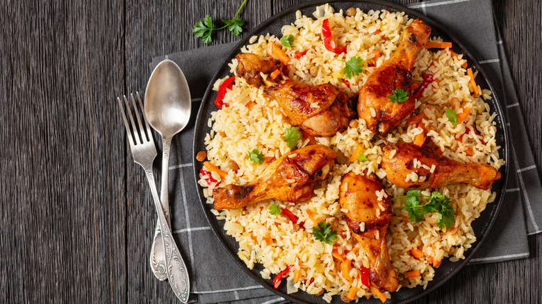 A plate of chicken pilaf with chicken drum sticks sitting on top next to silverware.