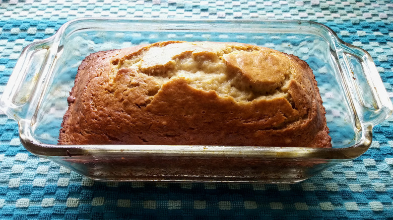 Banana bread in glass baking dish cooling on a kitchen towel