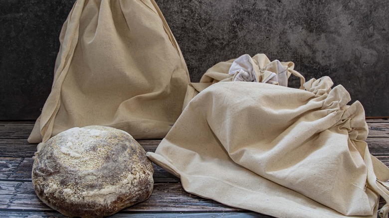 A loaf of artisan bread next to two linen bread bags