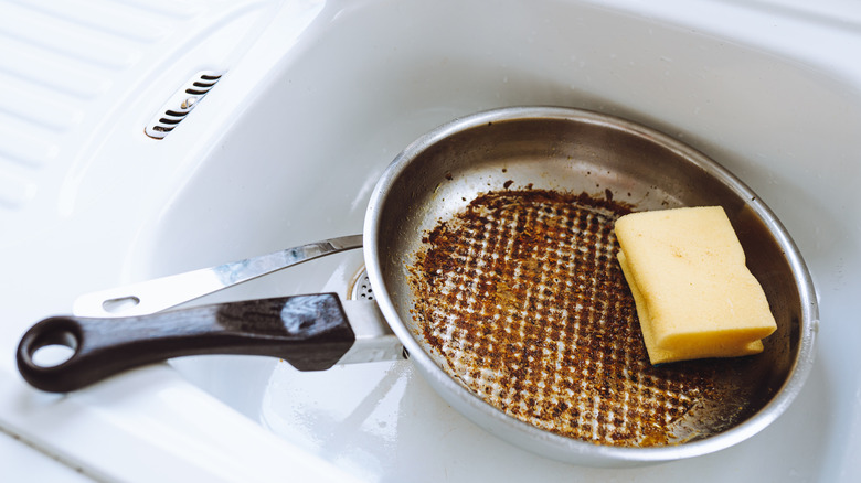 A dirty stainless steel pan in a sink with a sponge