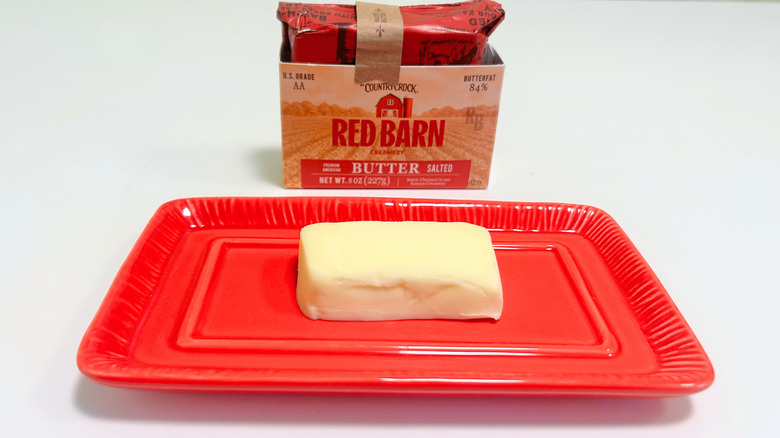 A box of Country Crock Red Barn Salted Butter next to a stick of butter on a red dish