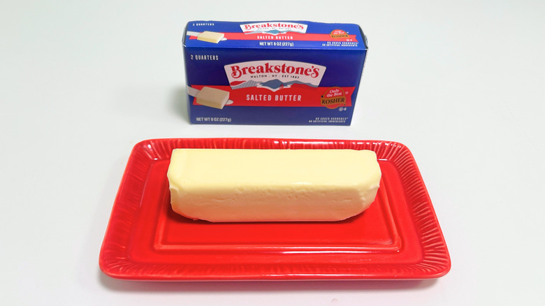 A box of Breakstone's Salted Butter next to a stick of butter on a red dish