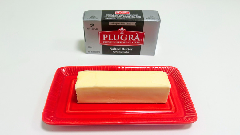 A box of Plugra Salted Butter next to a stick of butter on a red dish