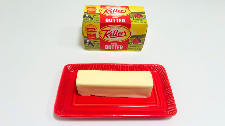 A box of Keller's Salted Butter next to a stick of butter on a red dish