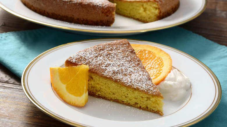 olive oil cake with orange slices and powdered sugar on a white and gold plate.