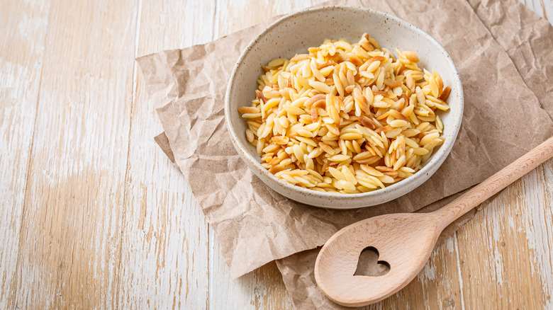 A bowl of orzo pasta with wooden spoon