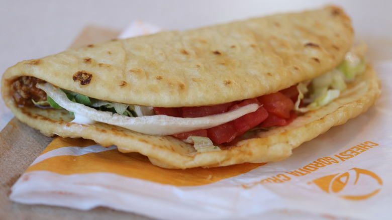 A Taco Bell chalupa laid out on its paper packaging on a wooden table