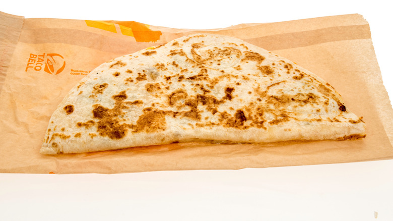 A Taco Bell quesadilla laid out on its paper wrapping against a white background