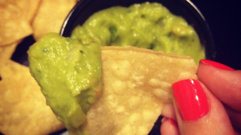 A close-up of a person holding a tortilla chip dipped in guacamole