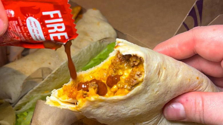 A person dumps Taco Bell Fire sauce over a beef and cheese burrito