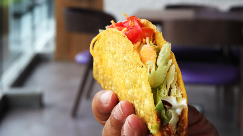 Hand holding taco outside Taco Bell