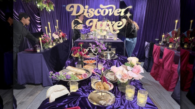 Items from the Taco Bell Luxe Value Menu set up on platters on a table with a purple velvet table cloth and a sign that says "Discover Luxe"