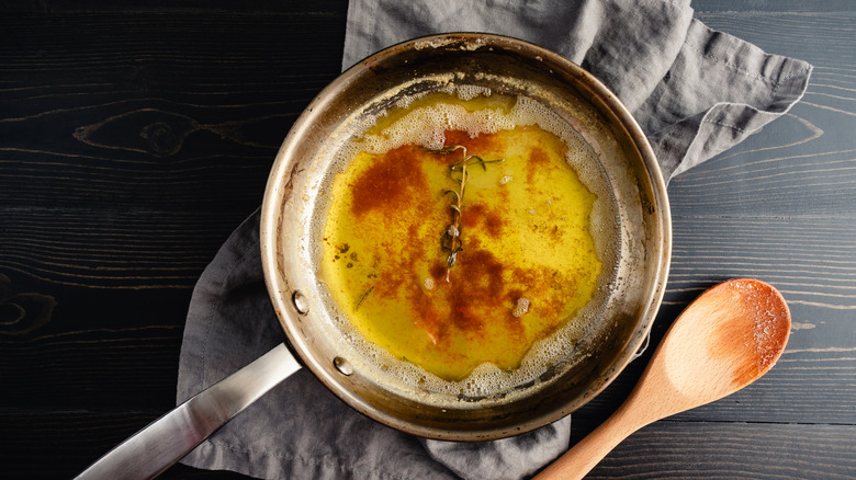 A skillet with brown butter and a rosemary sprig on a wooden table