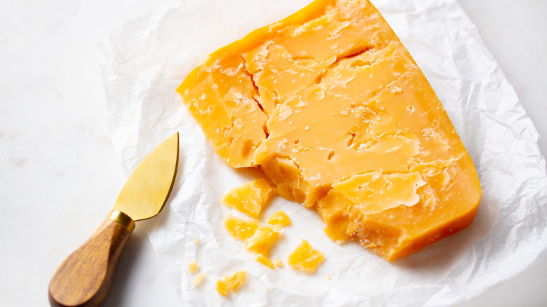 A block of cheddar cheese and a small cheese knife on a white table