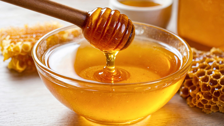 A glass bowl full of honey with a wooden dipper on a wooden table