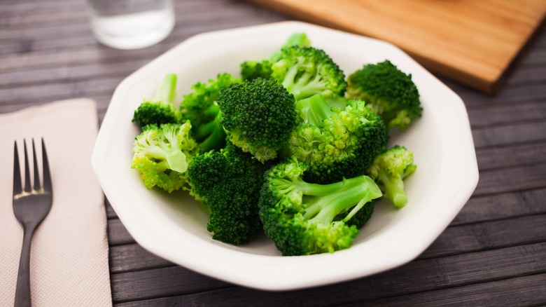 Steamed broccoli florets in a white plate placed on a wooden table