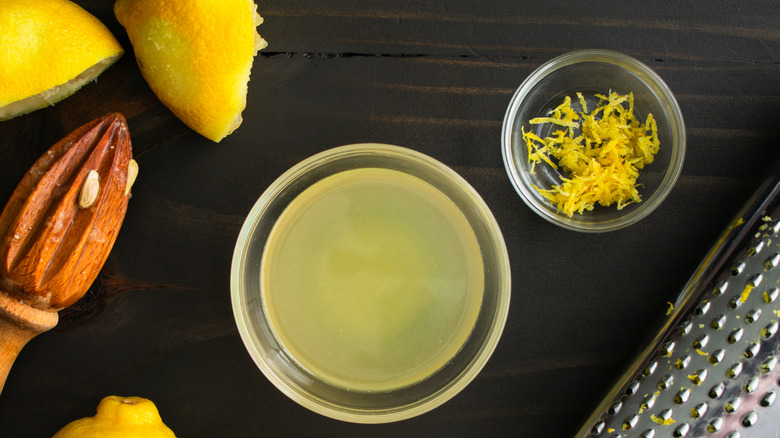 Lemon juice and zest in two separate glass bowls on a wooden table with fresh lemons