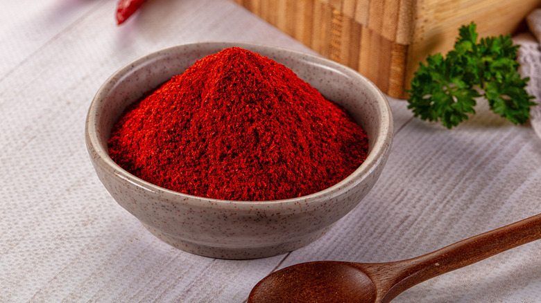 A bowl full of paprika on a table with a wooden spoon