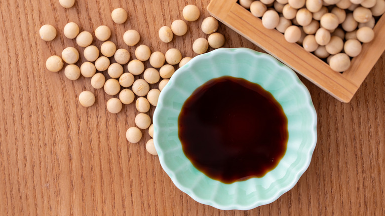 Soy sauce in a blue ceramic bowl on a wooden table with soy beans
