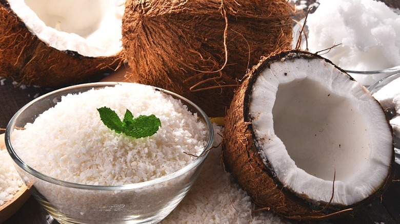 A bowl of coconut flakes surrounded by whole coconuts