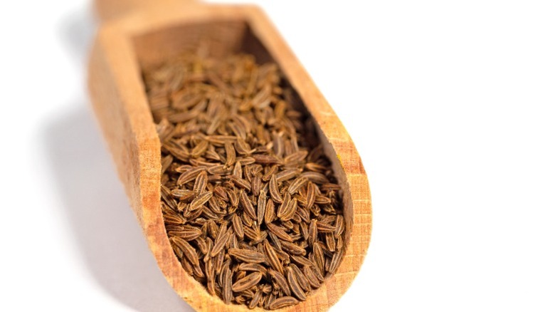 A wooden scoop with cumin seeds inside