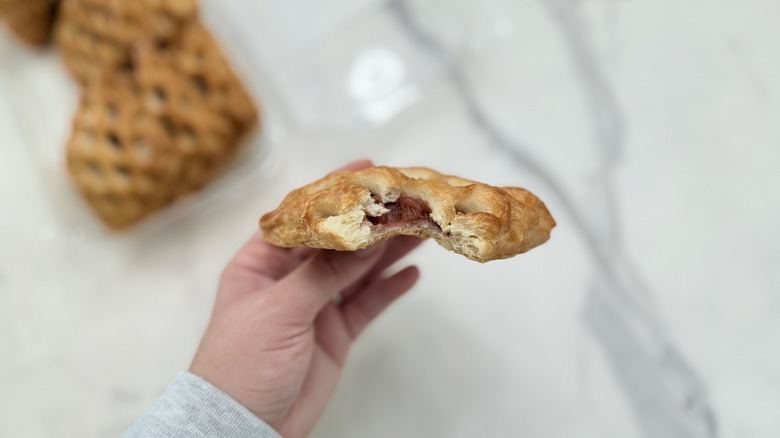 A strawberry rhubarb pastry with a bite taken out of it, showing the dark red filling