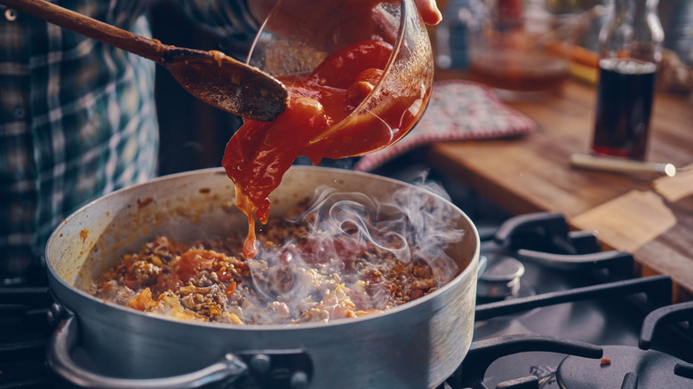 Person adding tomato sauce to Dutch oven