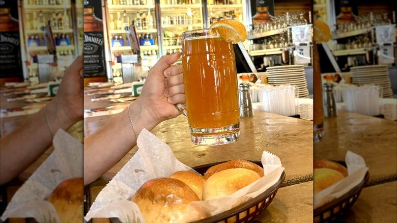 A hand holds a glass of beer above a basket of rolls in a Logan's Roadhouse