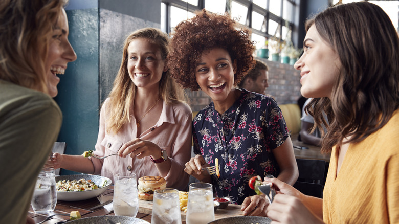 A group of friends are smiling and laughing while eating at a restaurant