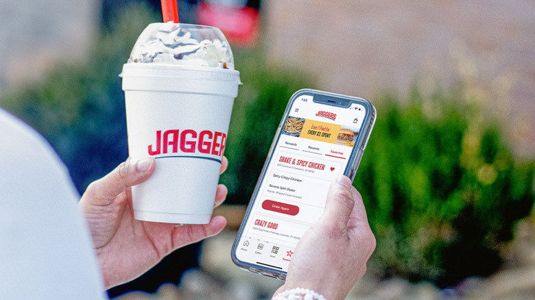 A customer holds a Jaggers milkshake with the rewards app displayed on their phone
