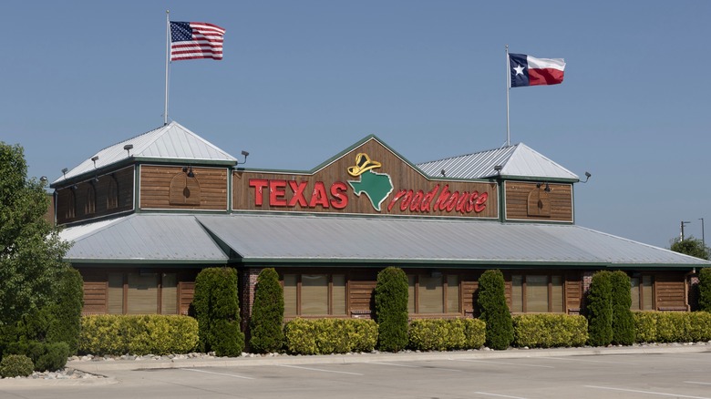 Exterior of a Texas Roadhouse location with two flags flying high above the building
