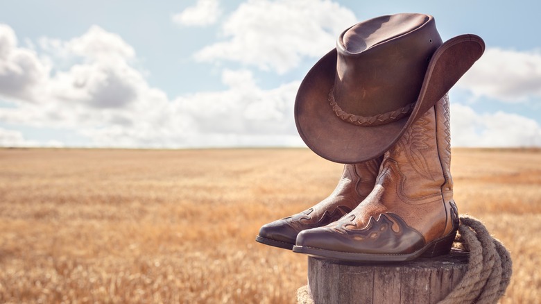 A cowboy hat and boots are neatly piled on a wooden post against blue sky