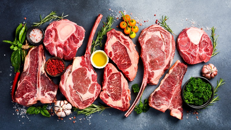 Various raw steak cuts with greenery against a steel colored background