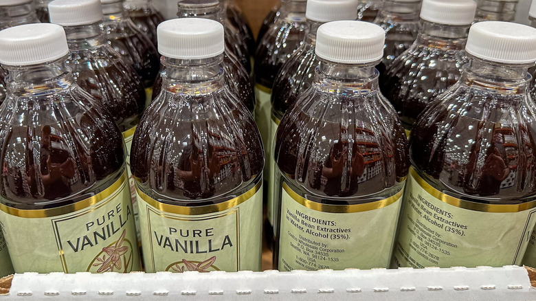 Pure vanilla extract in a bottle next to vanilla beans isolated on a white background