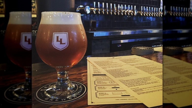 A goblet of beer next to a menu on the bartop of Loyal Legion bar in Portland airport