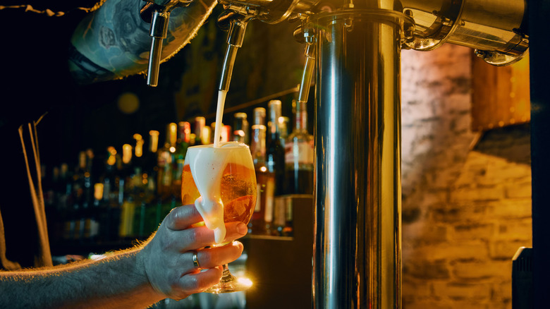 Foam spills over as a bartender fills a beer goblet from a tap