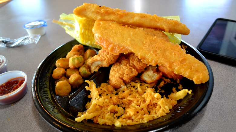 a plate of fried fish, fried okra, corn on the cob, and extra crispy bits from the fryer on a black Captain D's plate
