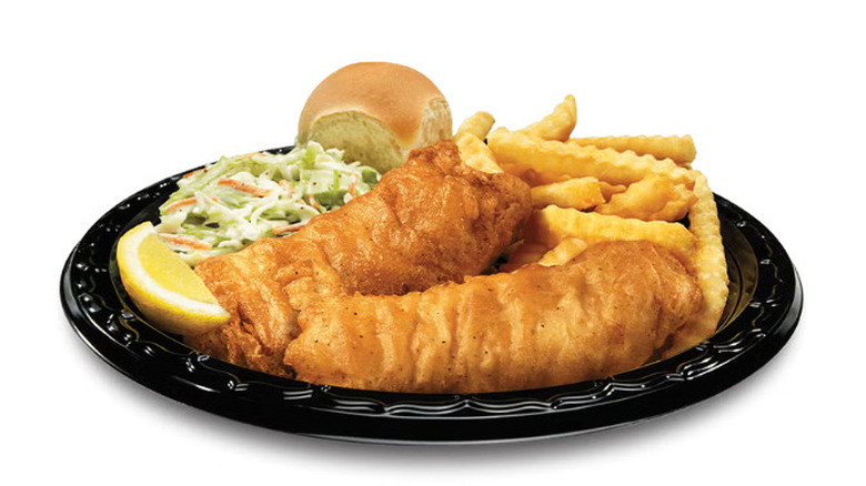 a plate of two pieces of fish, cole slaw, fries, a roll, and a lemon slice against a white background