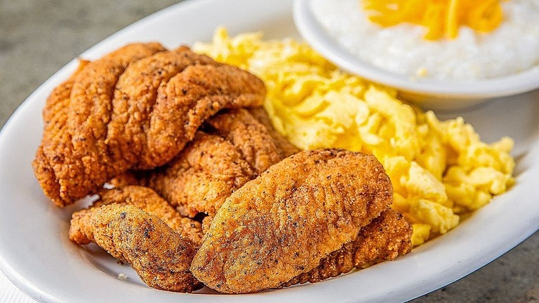 a plate of fried fish with scrambled eggs and a bowl of cheese grits