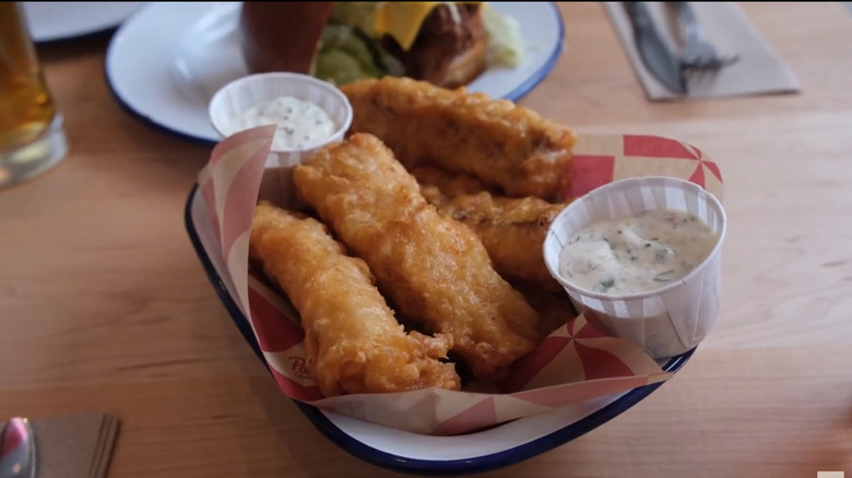a basket of fried fish with ramekins of tartar sauce