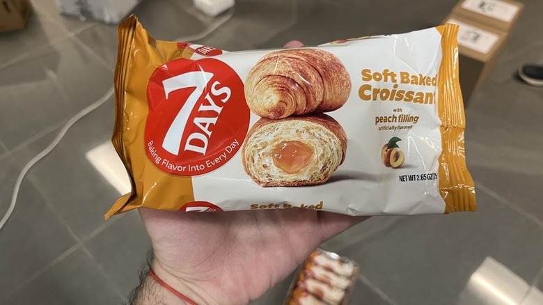 A hand holding a package of 7 Days Soft Baked Croissants w/ Peach Filling