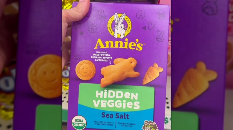 A hand holding a purple box of Annie's Organic Hidden Veggies Crackers w/ Sea Salt at Dollar Tree