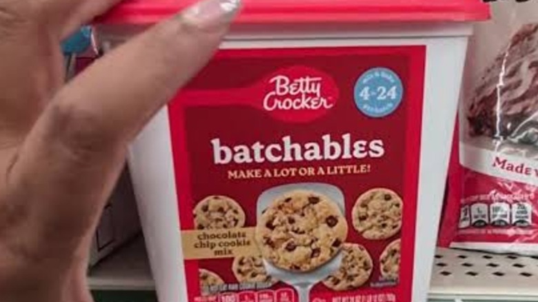 A hand holding a red tub of Betty Crocker Batchables Chocolate Chip Cookie Mix