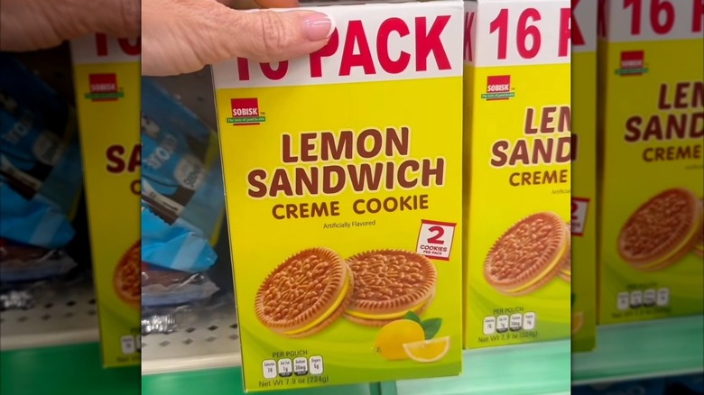 A hand holding a box of Dollar Tree Sobisk Lemon Sandwich Creme Cookies in a yellow box.