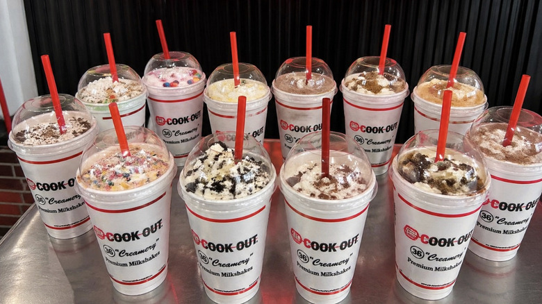 Twelve different flavors of Cookout shakes arranged in a circle with red straws in each cup