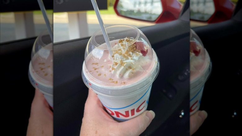 Hand holding a Sonic strawberry cheesecake shake in a car