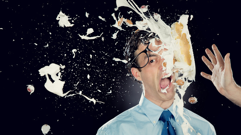 A man with glasses has a pie thrown in his face